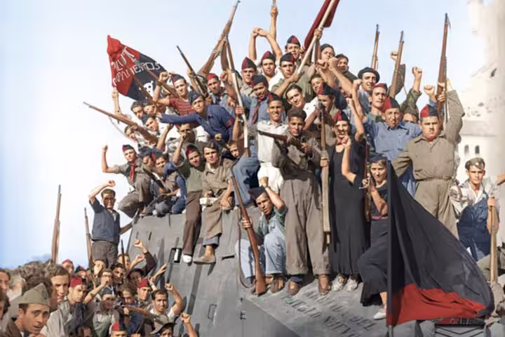 Historic photo of Spanish Civil War fighters with flags and rifles, highlighting Barcelona's revolutionary spirit.