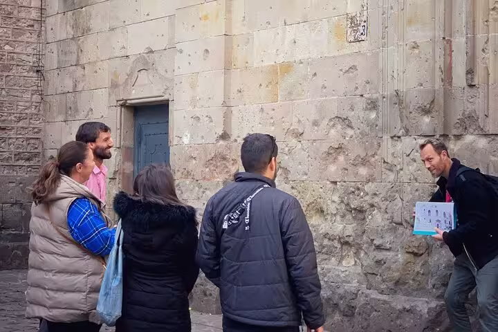Visitors observe a guide explaining bullet marks on a Barcelona building from the Spanish Civil War.