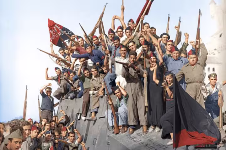 Crowd of Spanish Civil War soldiers with rifles and flags atop an armored vehicle in a historic wartime scene.