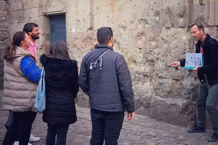 Tour guide explaining Spanish Civil War history to a group near a historic stone wall in Barcelona.
