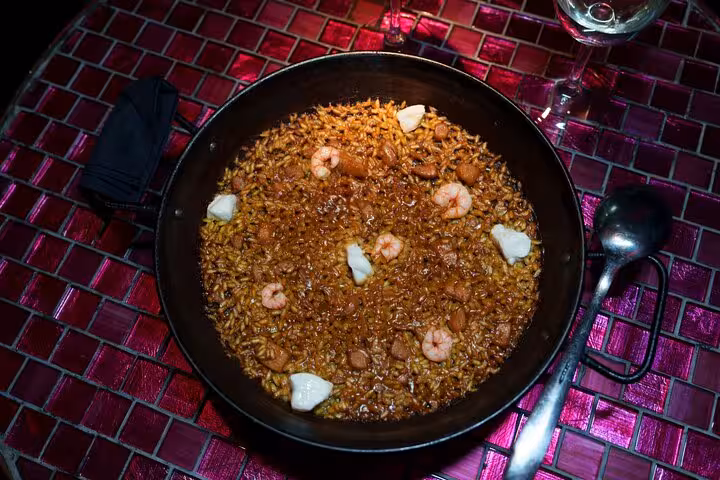 Close-up of a traditional Spanish paella dish with shrimp and aioli, served on a vibrant mosaic table in Barcelona.