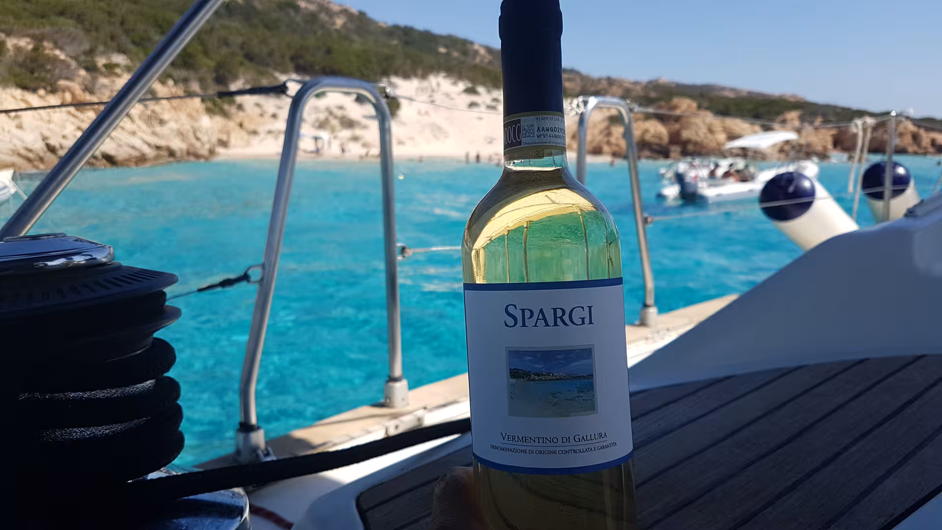 Bottle of Spargi wine on sailboat with stunning La Maddalena Archipelago beach view in the background.