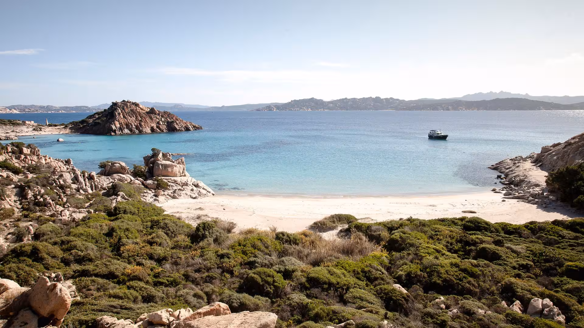 Scenic view of a secluded beach and crystal-clear sea with a boat in the La Maddalena Archipelago.