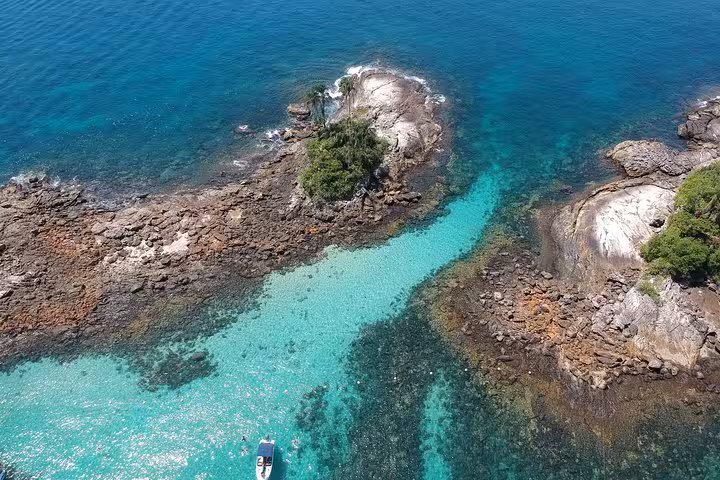 Aerial view of a speedboat navigating crystal-clear turquoise waters around rocky islets on a Paradise Island tour.