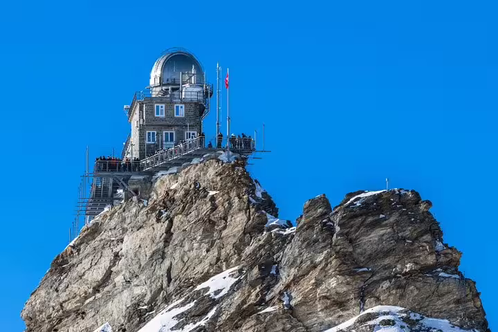 Stunning view of the Sphinx Observatory perched atop the snowy Jungfraujoch, under a clear blue sky.
