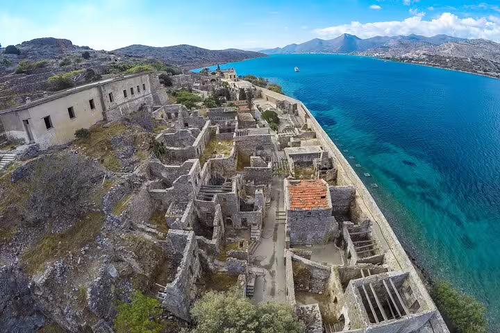 Aerial view of Spinalonga Island's historic ruins surrounded by turquoise waters on a sunny day in Crete.