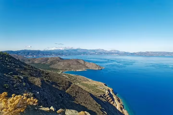 Panoramic view of the Mediterranean coastline near Spinalonga with rugged cliffs and deep blue sea under a bright sky.