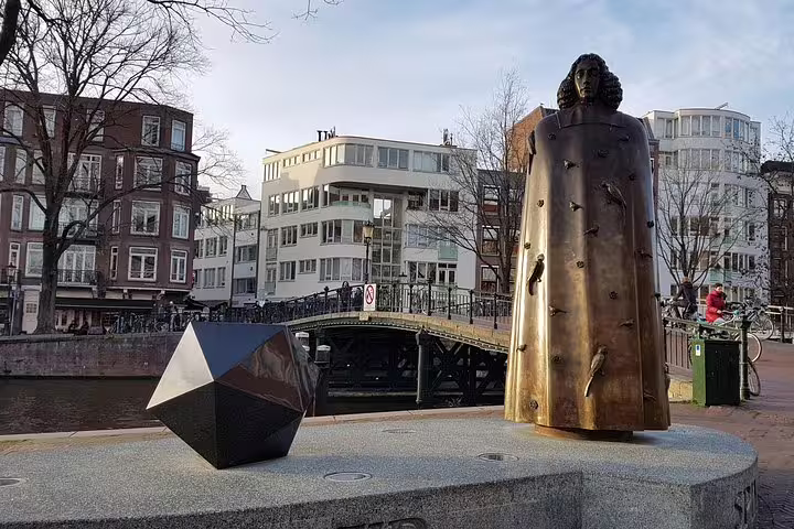 Statue of Spinoza near a canal bridge in Amsterdam's Jewish Quarter, highlighting cultural heritage on a private tour.