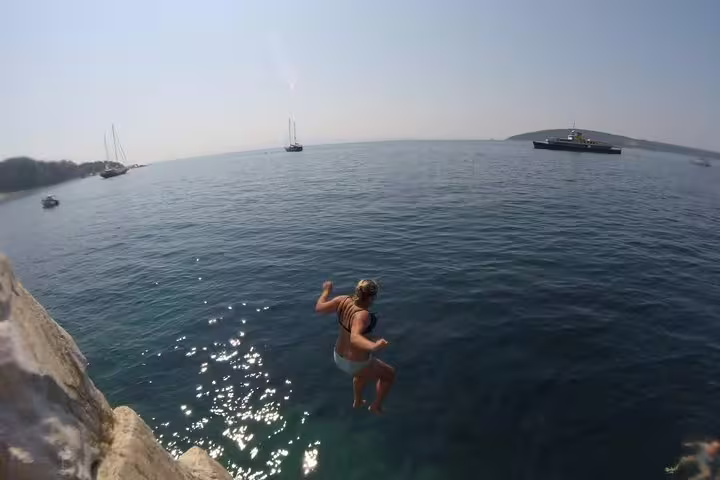 Traveler cliff jumping into clear Adriatic near Split, Croatia, during sea kayaking and snorkeling tour stop
