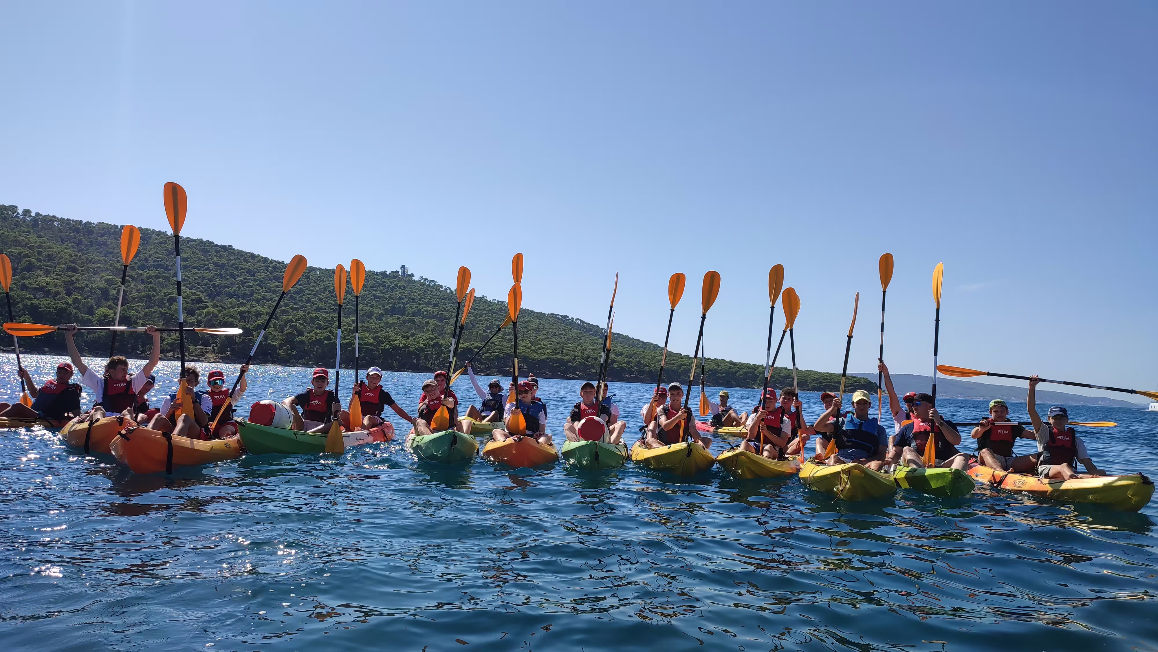 Large group sea kayaking in Split on the Adriatic, raising paddles near Marjan Hill before snorkeling break