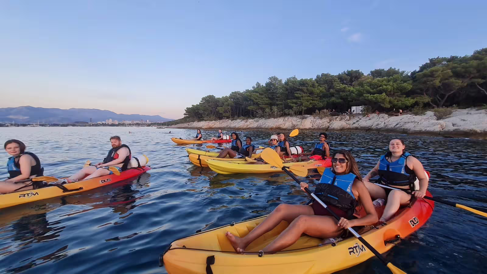 Happy group in yellow kayaks on a Split sea kayaking and snorkeling tour along a pine-lined Adriatic coast