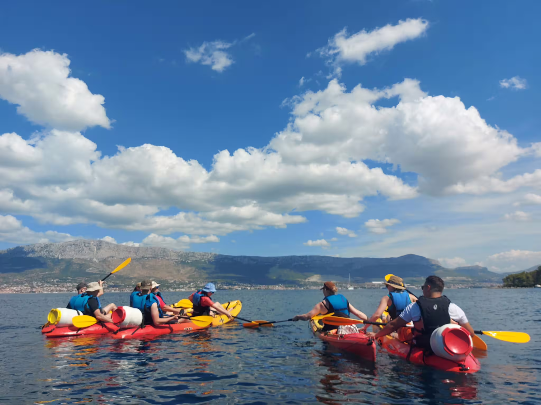 Group sea kayaking near Split with red kayaks on calm Adriatic water, scenic mountains on a guided tour