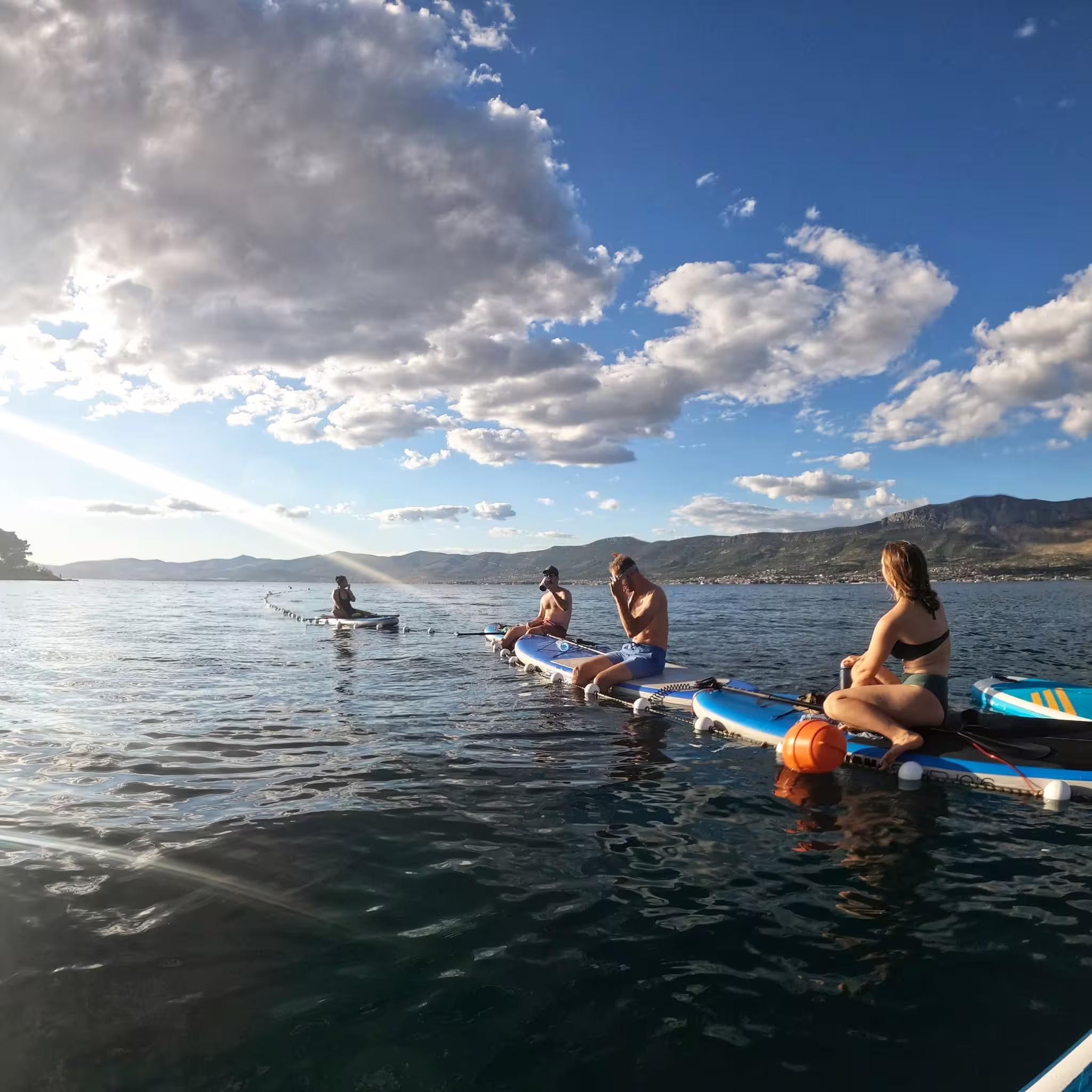 Group relaxing on SUP boards on the Adriatic during a Split stand up paddle tour with mountain views