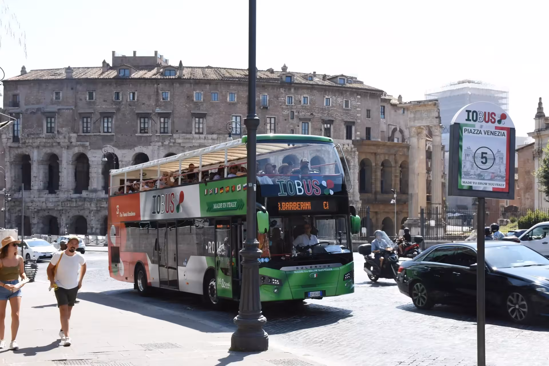 Open-top tour bus passing by Piazza Venezia, showcasing historic architecture on the Squares and Fountains Combo Tour.