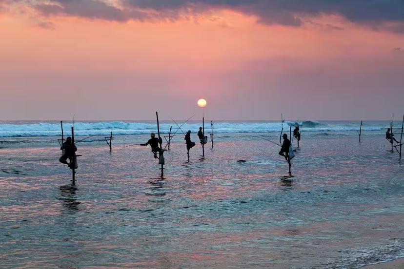 Silhouettes of traditional stilt fishermen at sunset on Sri Lanka's scenic coast, showcasing cultural heritage and serene beauty.