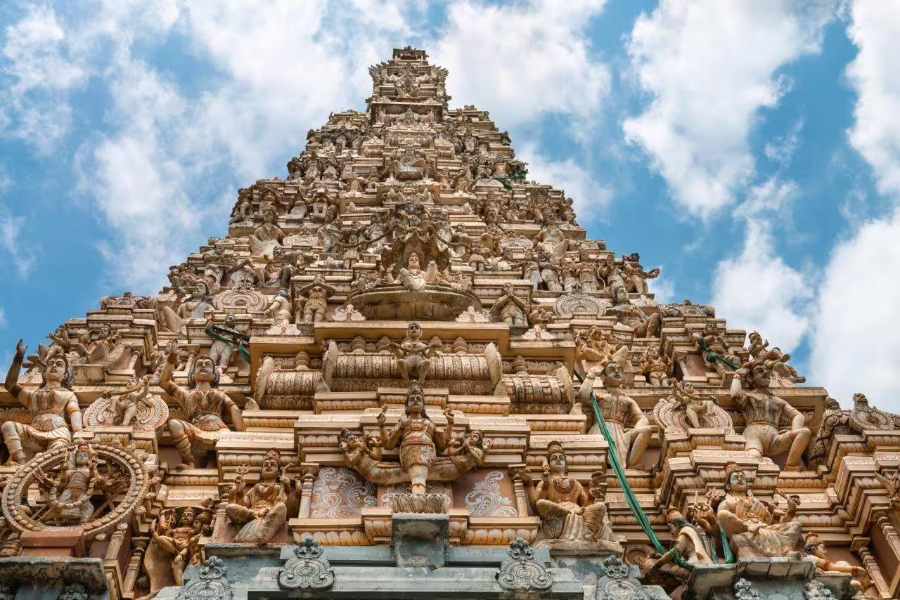Intricate carvings of Hindu deities on a towering Sri Lankan temple gopuram under a clear blue sky.