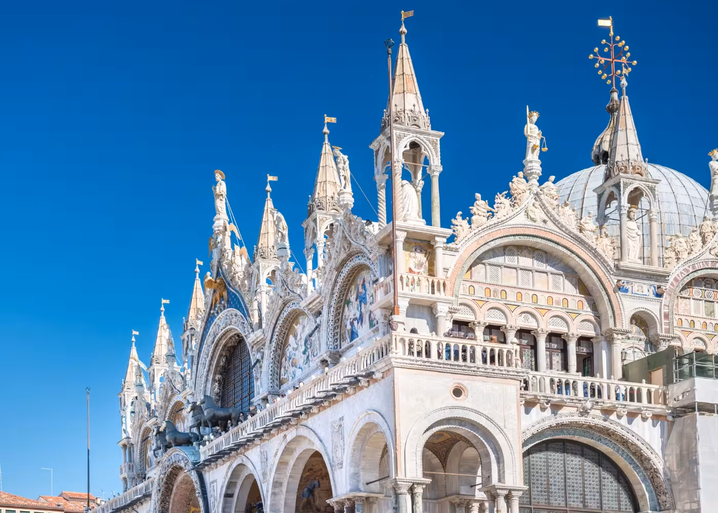 Stunning facade of St. Mark's Basilica with ornate arches and sculptures under a clear blue sky in Venice.