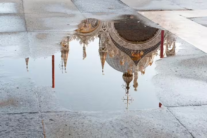 Reflection of St Mark's Basilica domes in a puddle, capturing Venice's architectural beauty on a luxury tour.