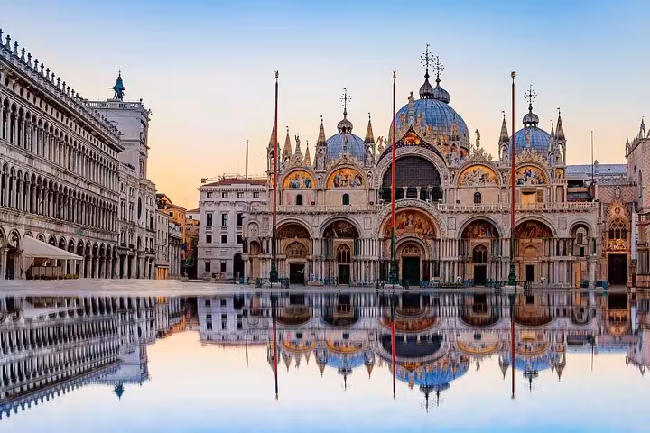Stunning view of St. Mark's Basilica reflecting in water at sunrise, perfect for a Venice day trip from Florence.