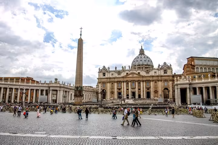 Daytime view of St. Peter's Basilica and the obelisk with tourists exploring Vatican City, perfect for a dome climb tour.