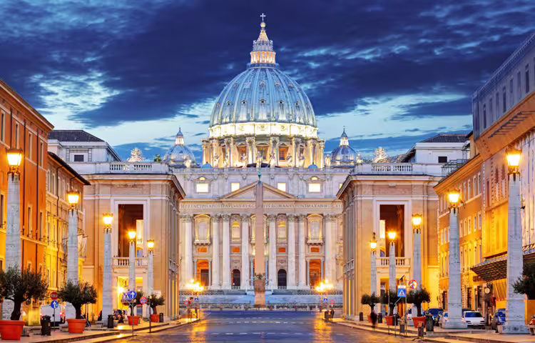 Illuminated façade of St Peter’s Basilica at dusk, landmark highlight of Rome Angels and Demons half‑day tour