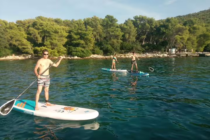 Stand up paddle tour near Split coastline, paddlers on SUP boards by pine forest and clear Adriatic water
