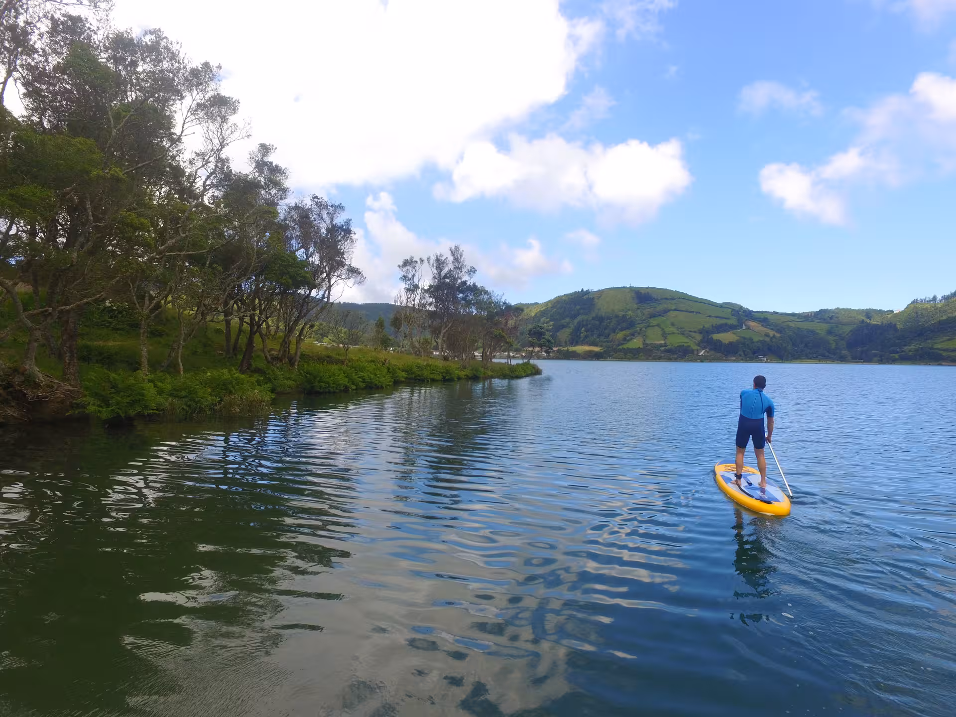 Stand up paddleboarder glides across a peaceful lake bordered by forested hills, ideal for relaxing SUP tours.