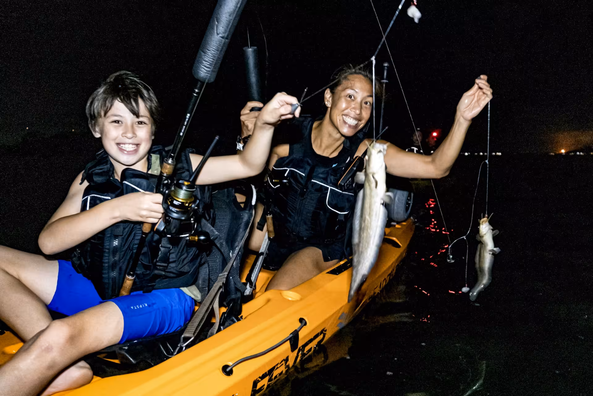 Smiling duo in a kayak showcasing their catch from the starry night fishing tour at Pulau Ubin.