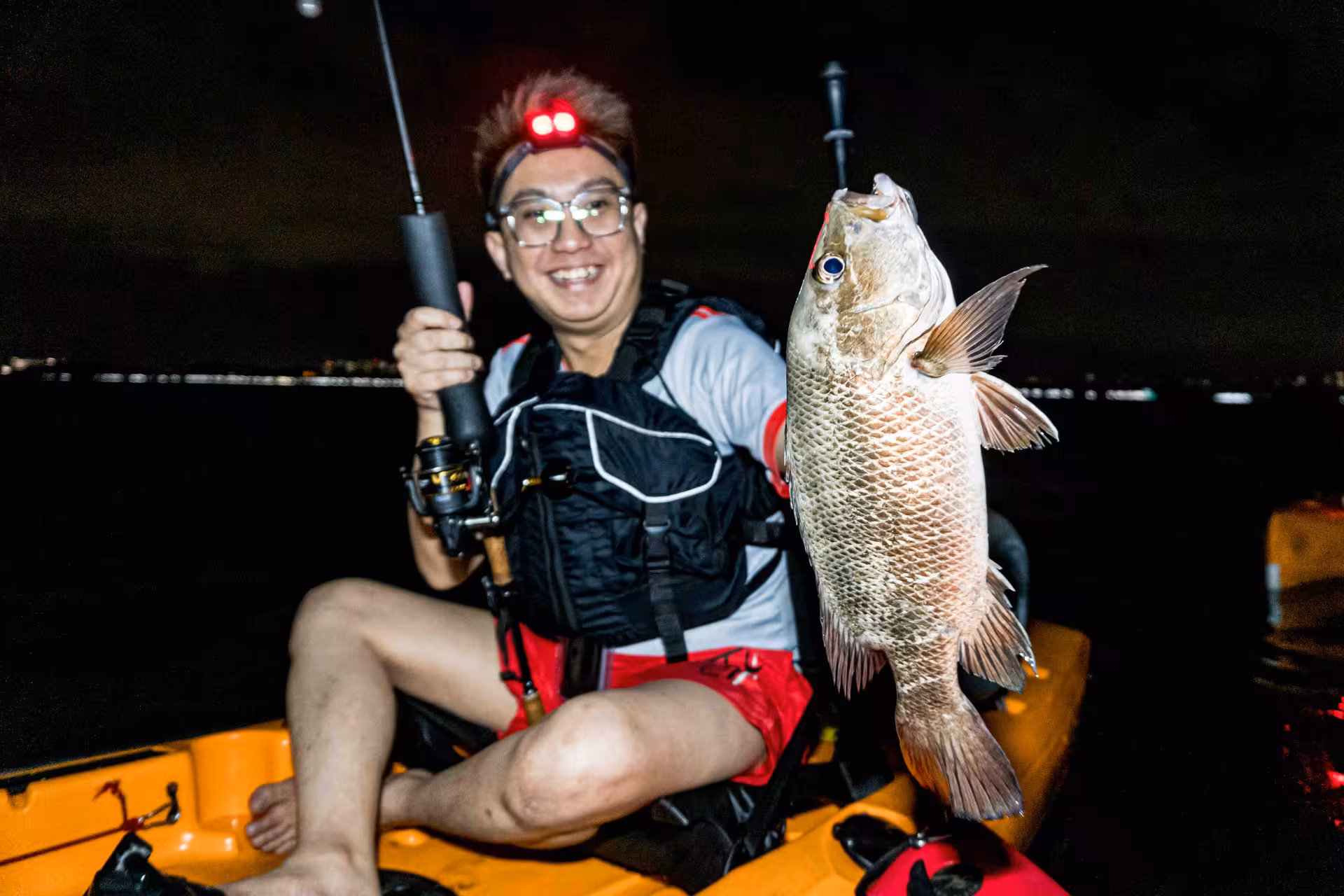 Smiling angler in kayak proudly holds up a freshly caught fish during nighttime fishing adventure at Pulau Ubin.
