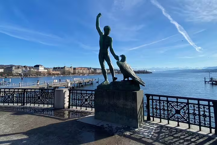 Statue overlooking Lake of Zurich with clear blue skies, offering a picturesque view of the waterfront.
