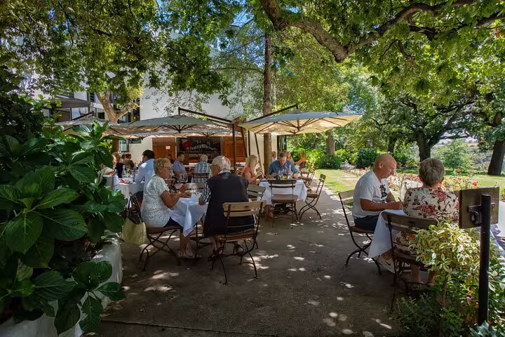 Guests enjoy outdoor dining under umbrellas at a lush Stellenbosch winery on the Full-Day VIP Wine Tour.