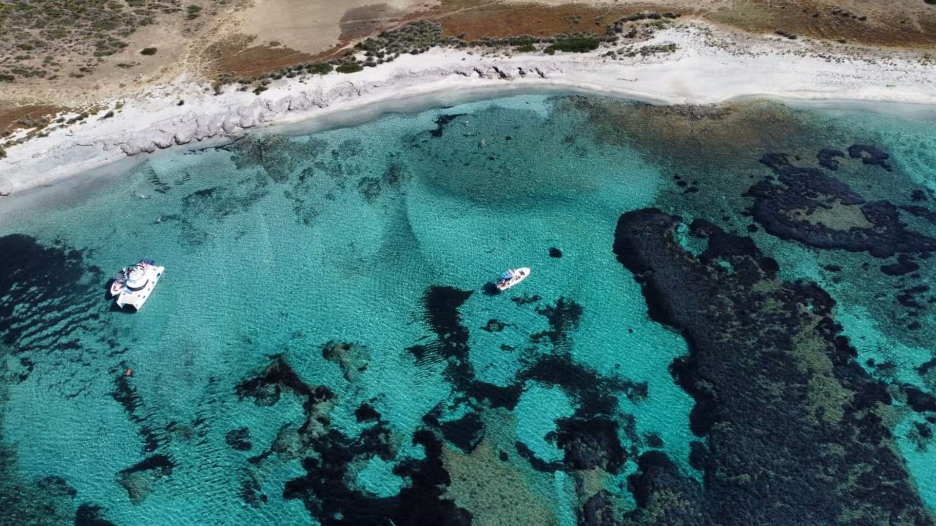 Drone shot of boats anchored in turquoise waters along a sandy beach during Stintino to Asinara boat excursion.