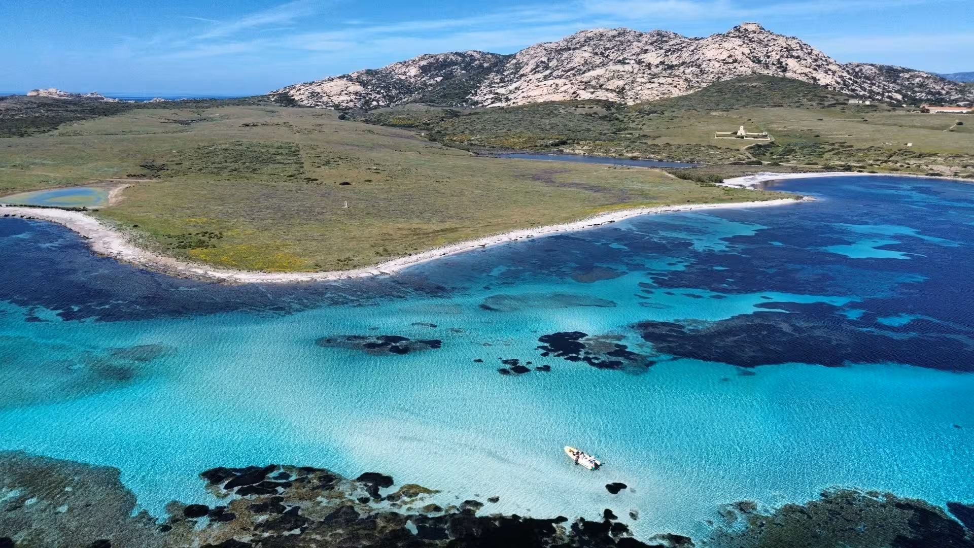 Pristine waters and rugged landscape of Asinara Island with a dinghy, highlighting the allure of Stintino excursions.