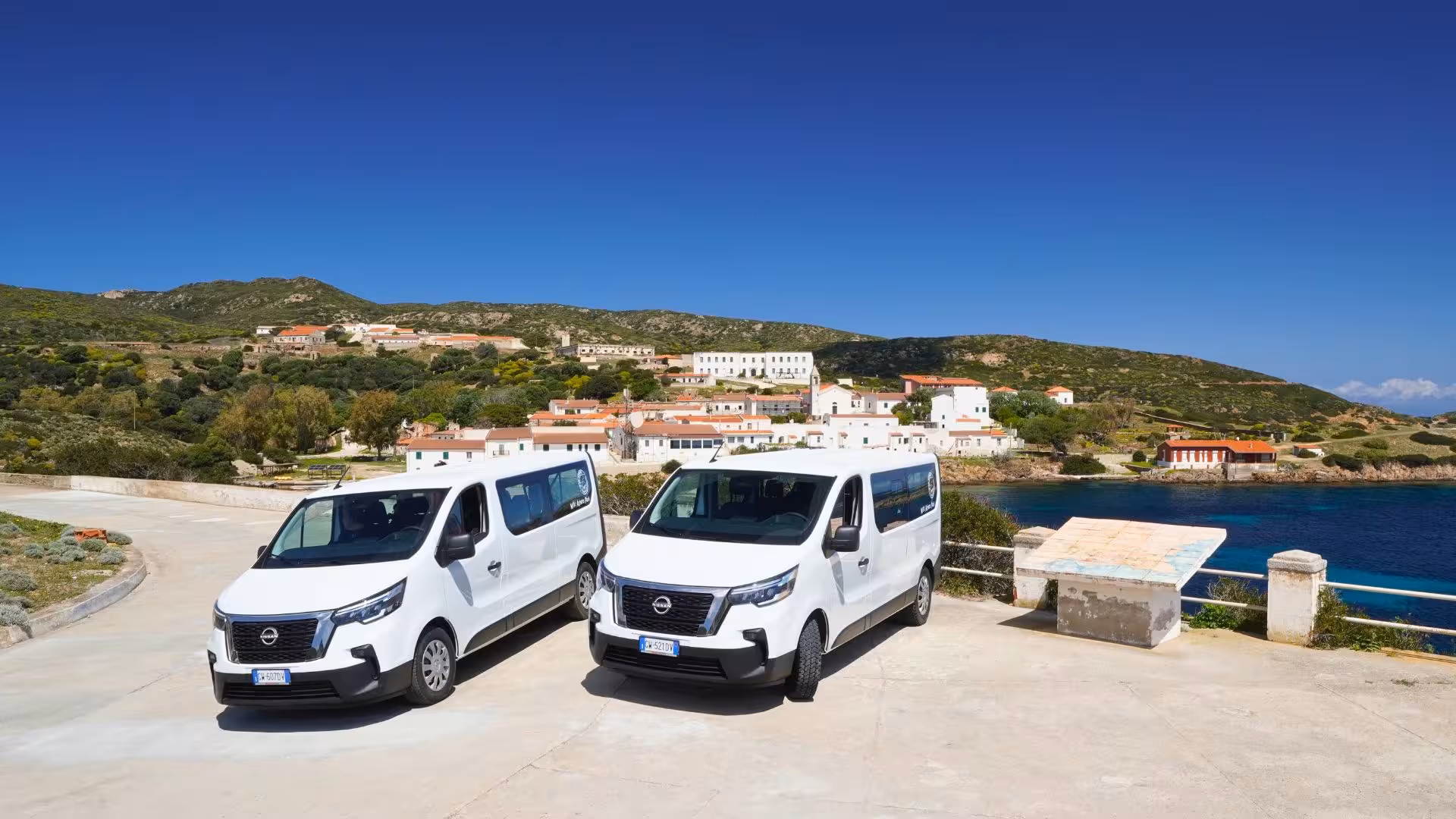 Two minivans parked with scenic Asinara village and coastline view, perfect for the Stintino island tour.