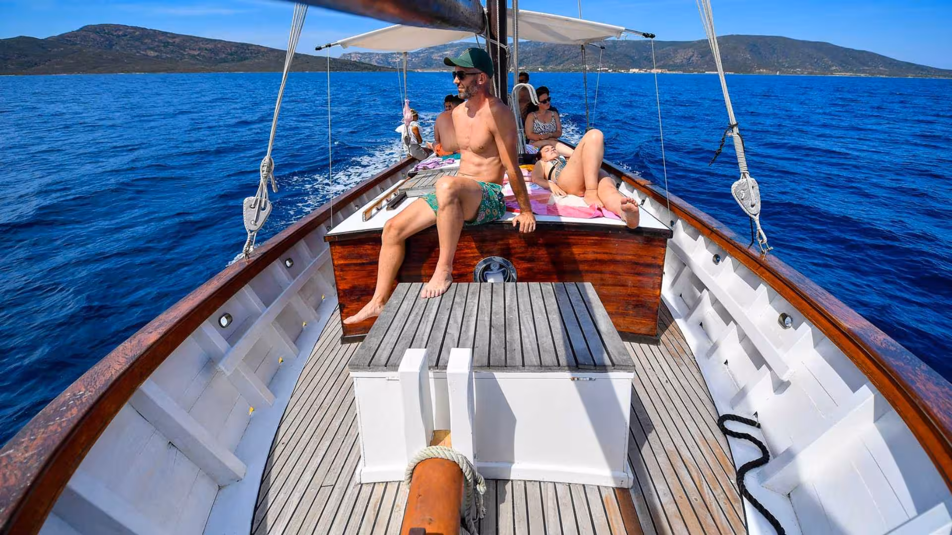 Relaxed tourists sunbathing on a sailboat deck during a scenic cruise from Stintino to Asinara Island.