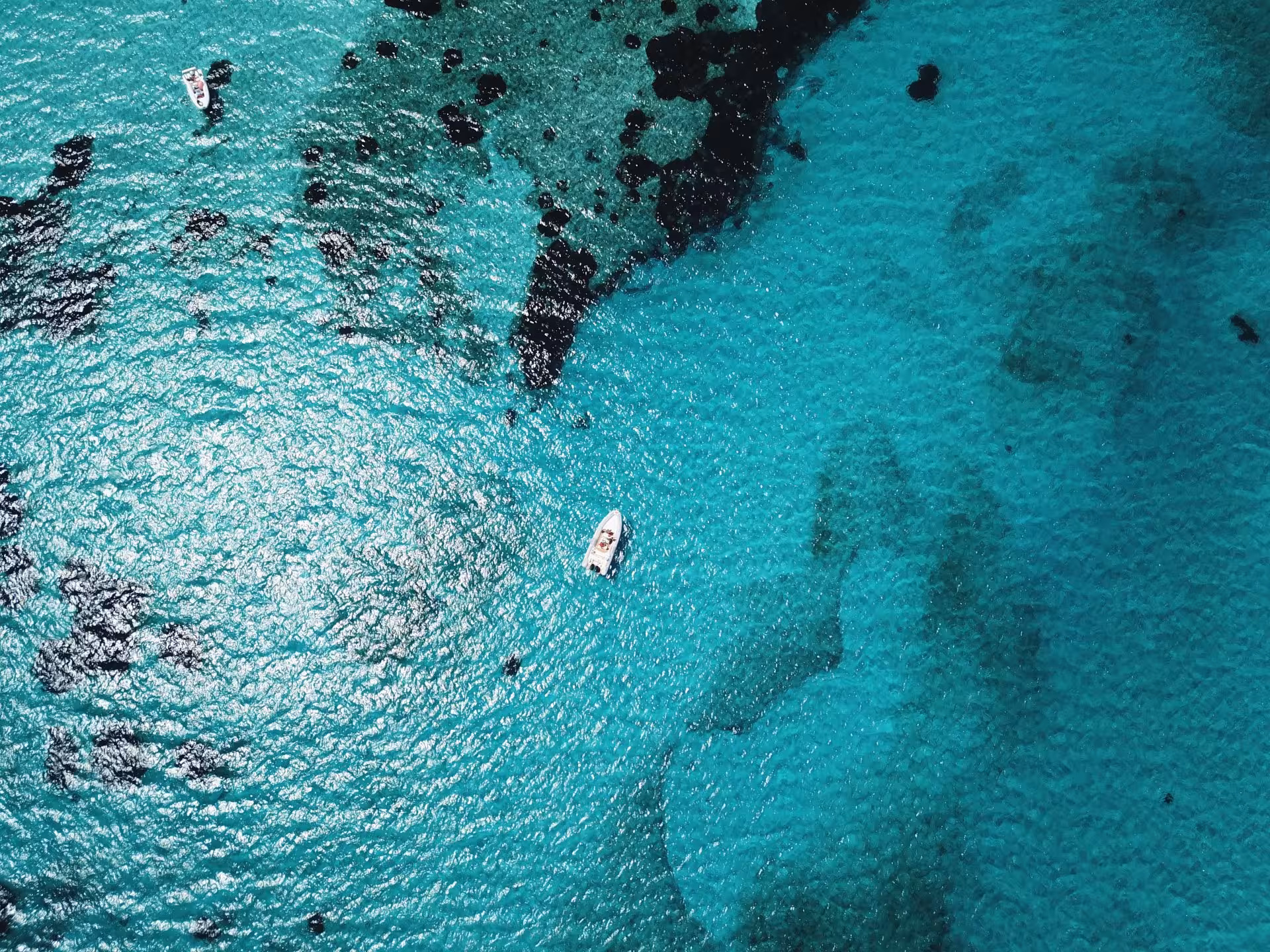 Aerial view of boats navigating the sparkling turquoise waters and dark patches of the Asinara Gulf.