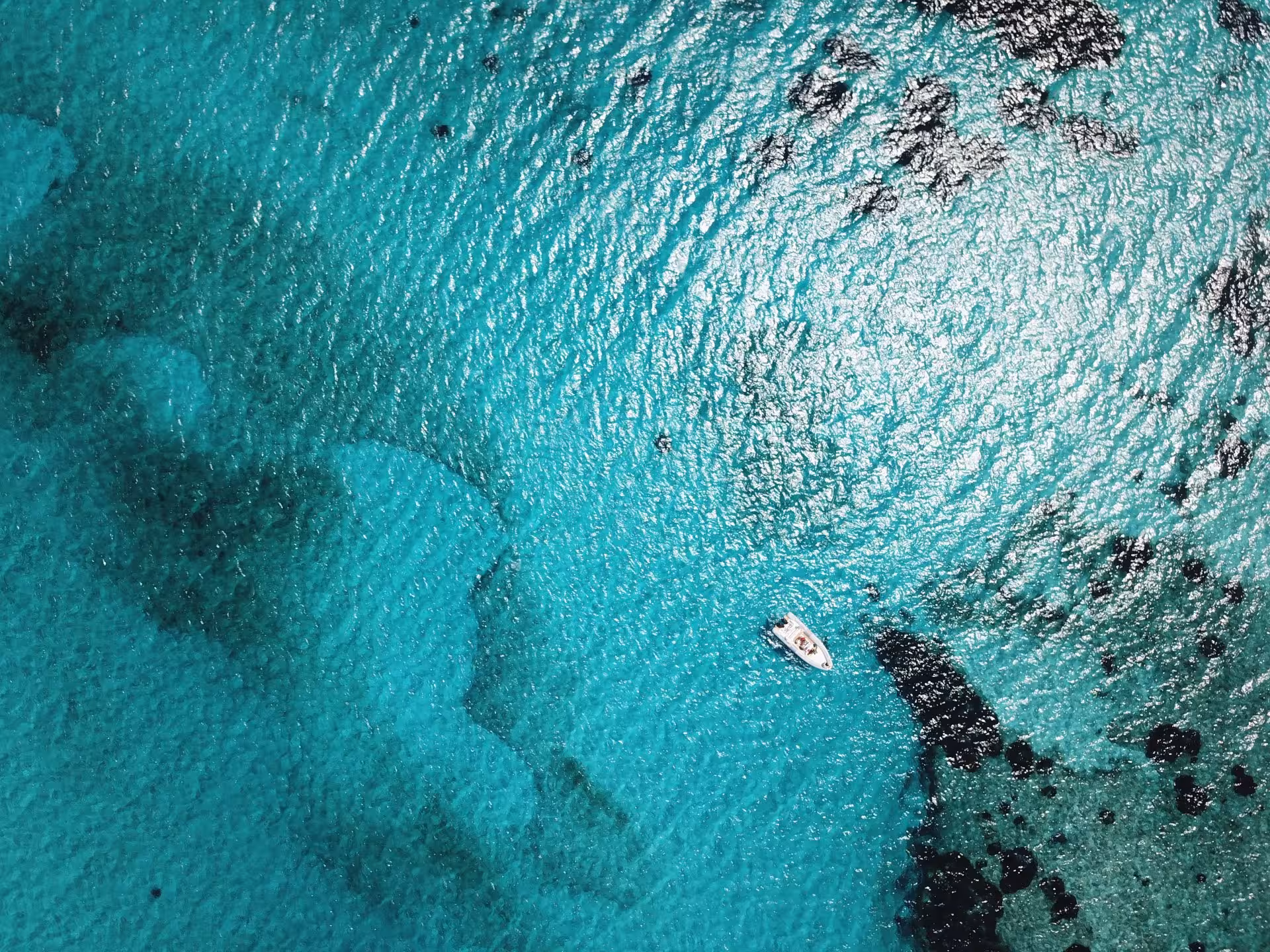 Drone captures a solitary boat amidst the shimmering blue and black speckled waters of the Asinara Gulf.