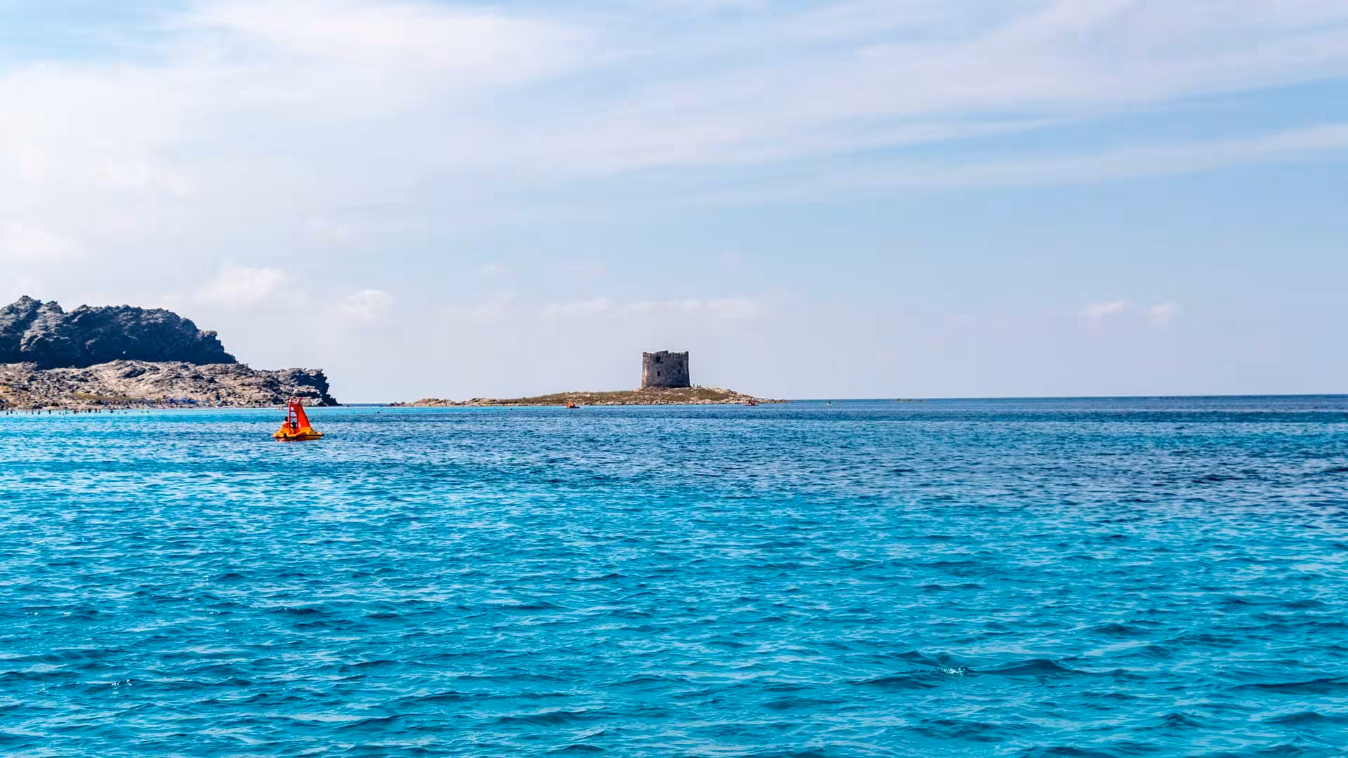 View of Asinara's azure waters and historic tower, ideal for a Stintino sailboat tour adventure.