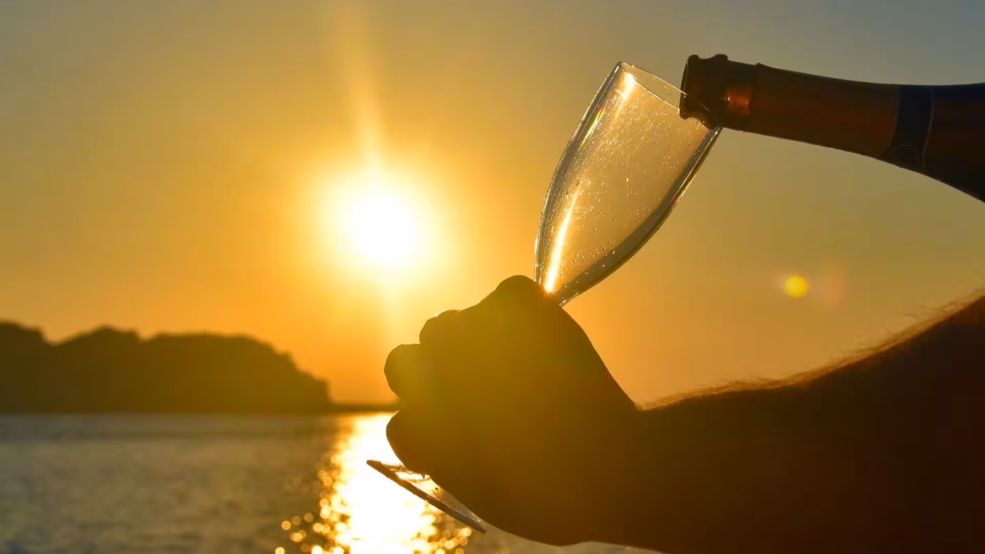 Champagne being poured into a glass against a stunning sunset on a Stintino catamaran tour in the Gulf of Asinara.