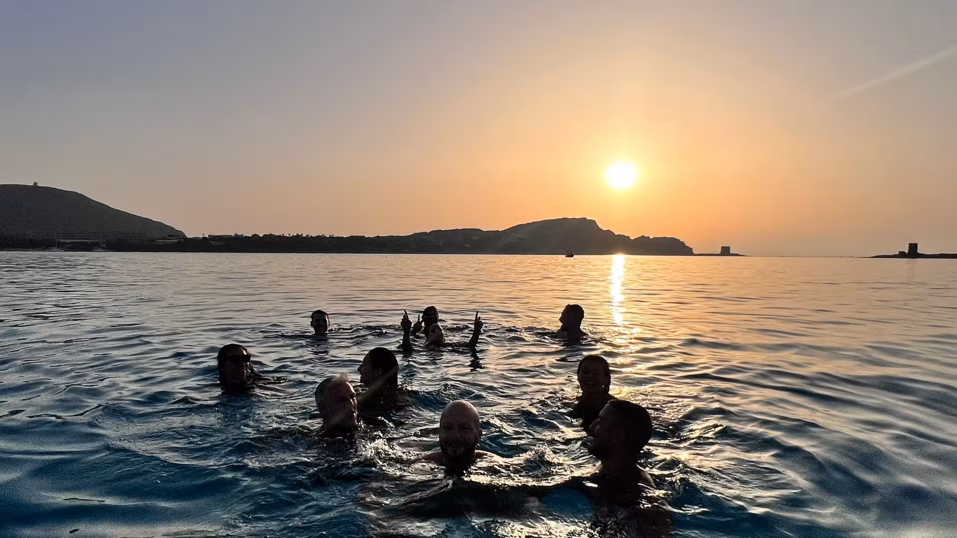 Group of people enjoying a swim at sunset in the Gulf of Asinara on a Stintino catamaran tour, with scenic views.