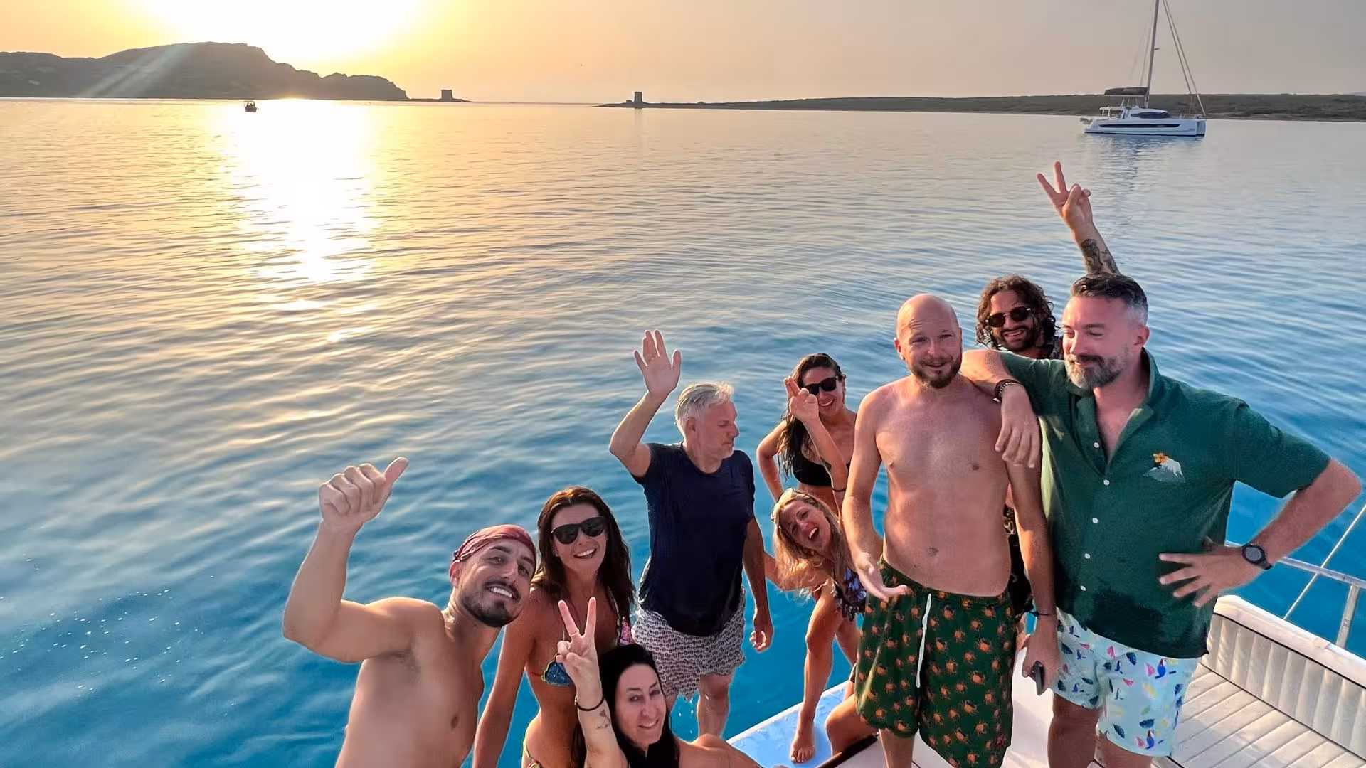 Happy group posing on a catamaran at sunset in the Gulf of Asinara, part of a Stintino sunset tour experience.