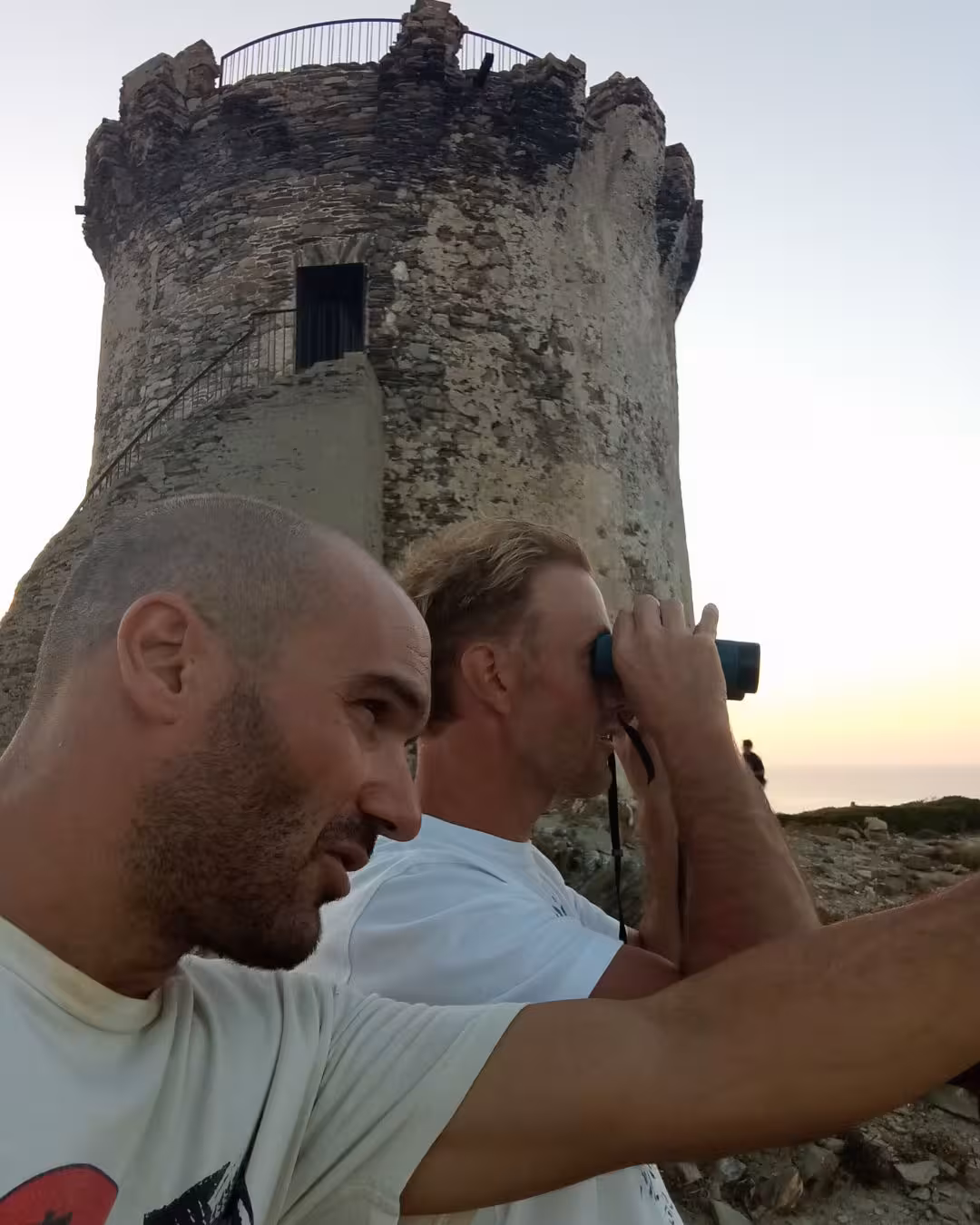 Visitors enjoy sunset views with binoculars at Capo Falcone tower during Stintino hike and tasting tour.
