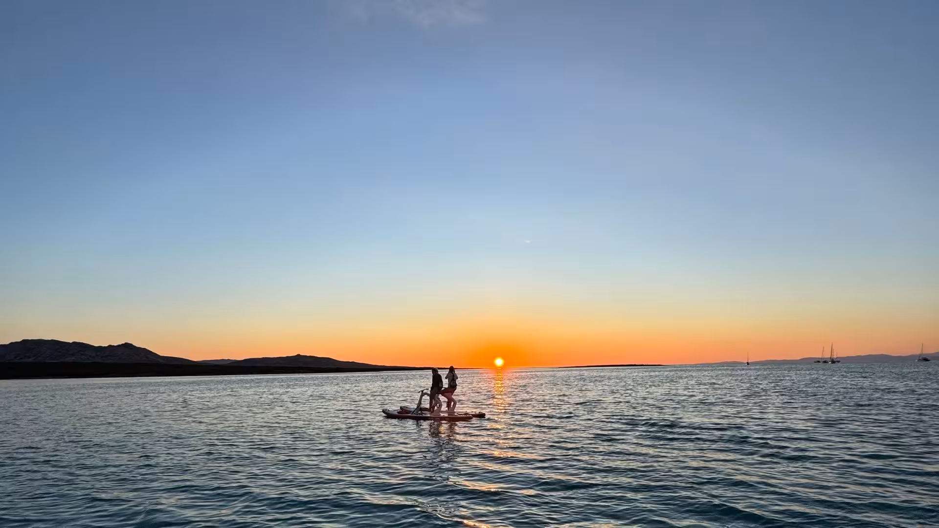 Two people enjoy a water bike ride at sunset on La Pelosa Beach, Stintino, with a stunning horizon view.