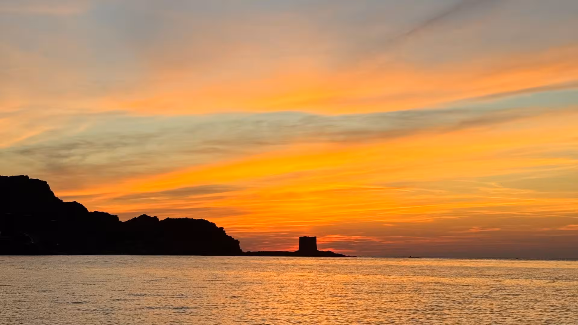 Vibrant sunset over La Pelosa Beach in Stintino, highlighting the iconic silhouette of a coastal tower.