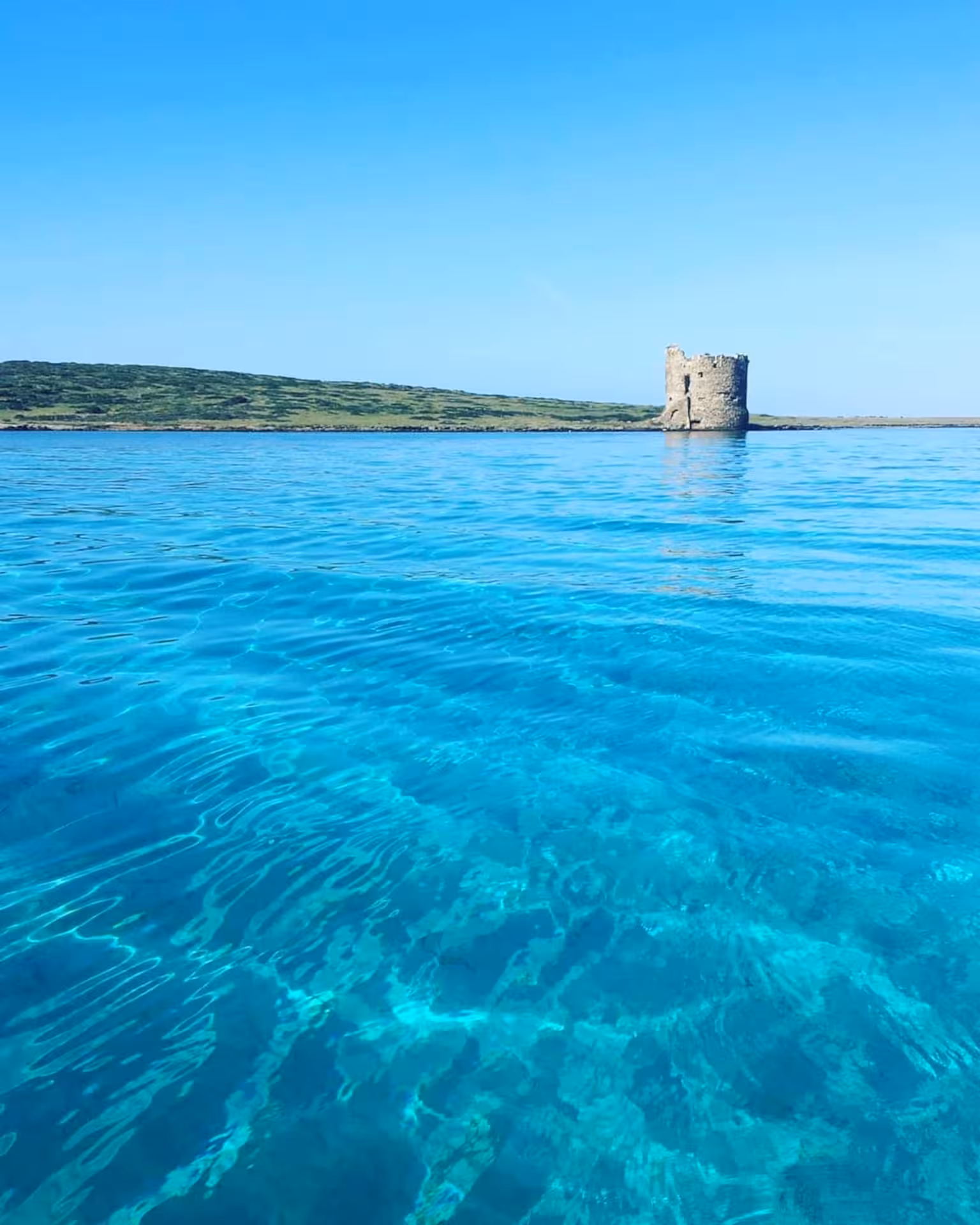 View of Asinara Island's turquoise waters and historic coastal tower on a wooden boat excursion from Stintino.