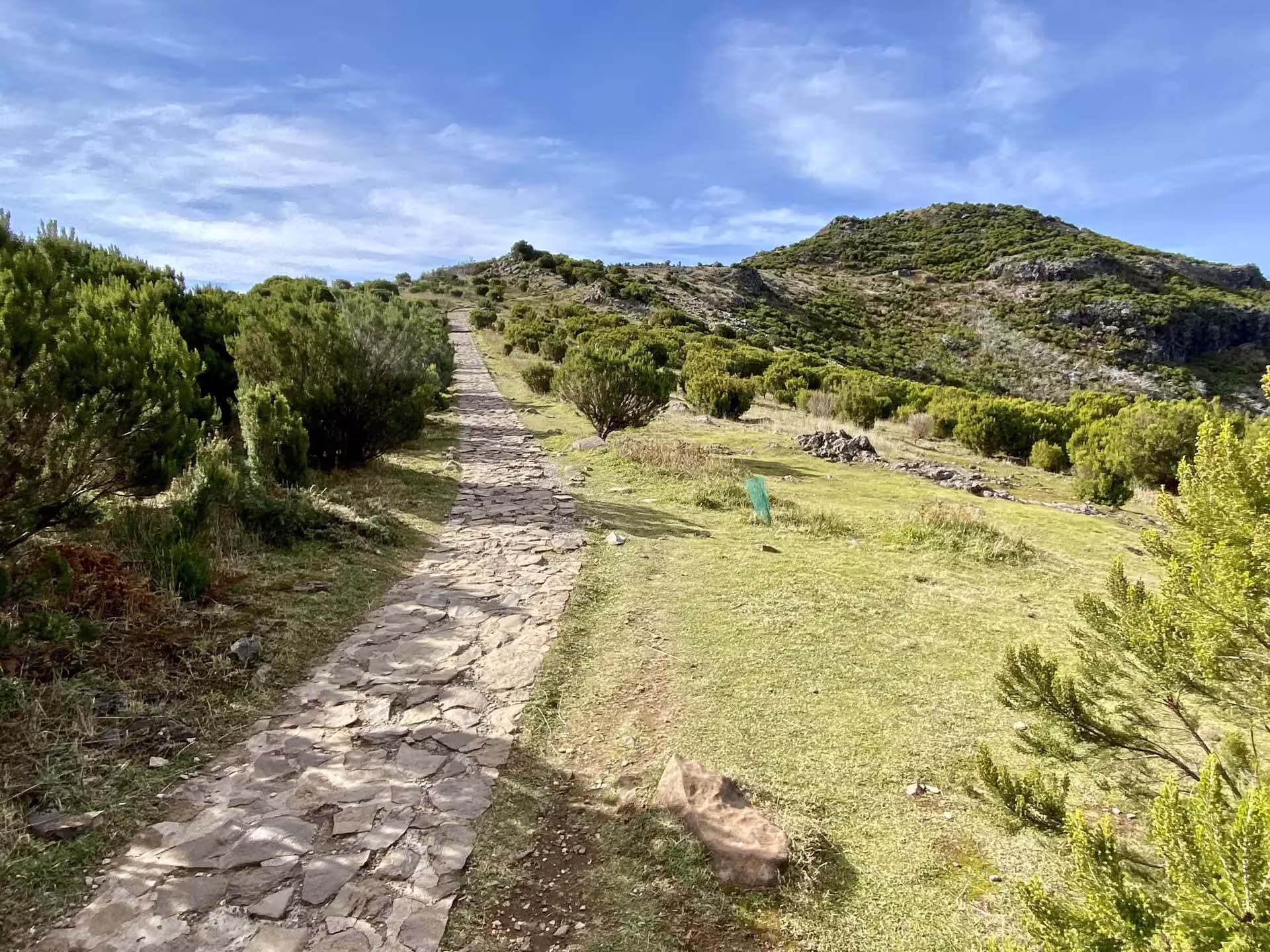 Stone path winding through lush green hills under a clear blue sky on Above the Skies' Hike tour.