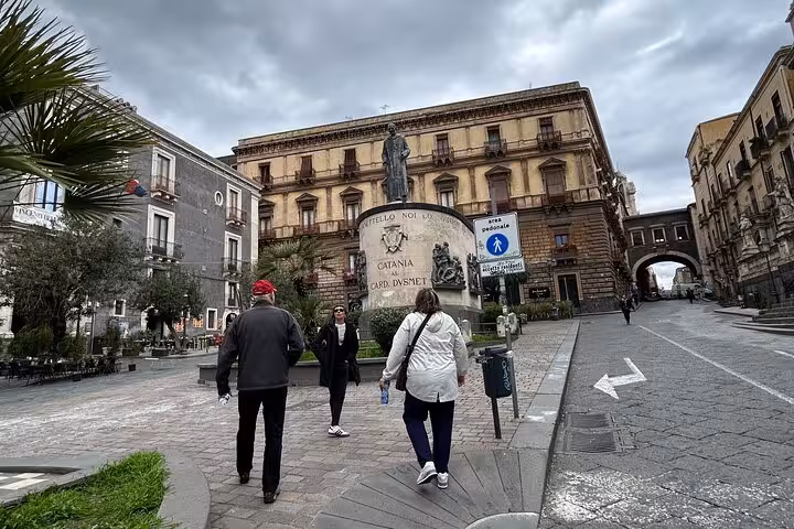 Tourists explore Piazza Carlo Alberto in Catania, surrounded by historic architecture on a cloudy day.