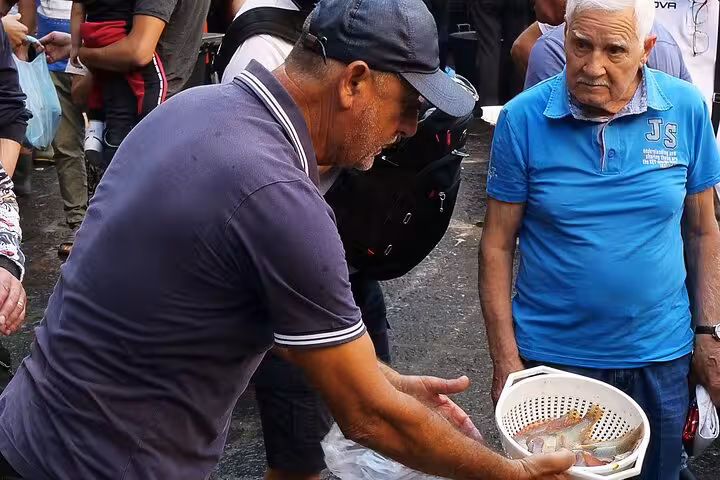 Street vendor showcasing fresh seafood to a customer at a bustling Catania market, highlighting authentic local culture.