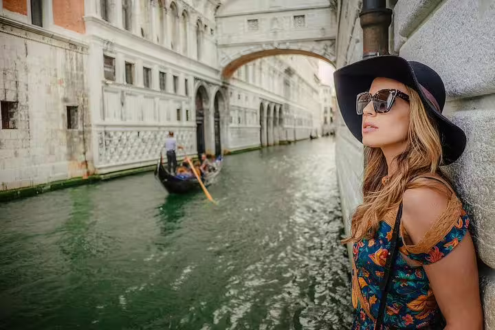 Stylish woman poses by Venice canal with gondola in background during private photo shoot and walking tour.