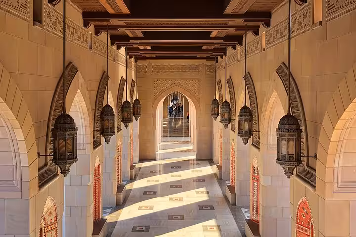Golden light over arched corridor and lanterns of Sultan Qaboos Grand Mosque on Muscat evening sightseeing taxi tour